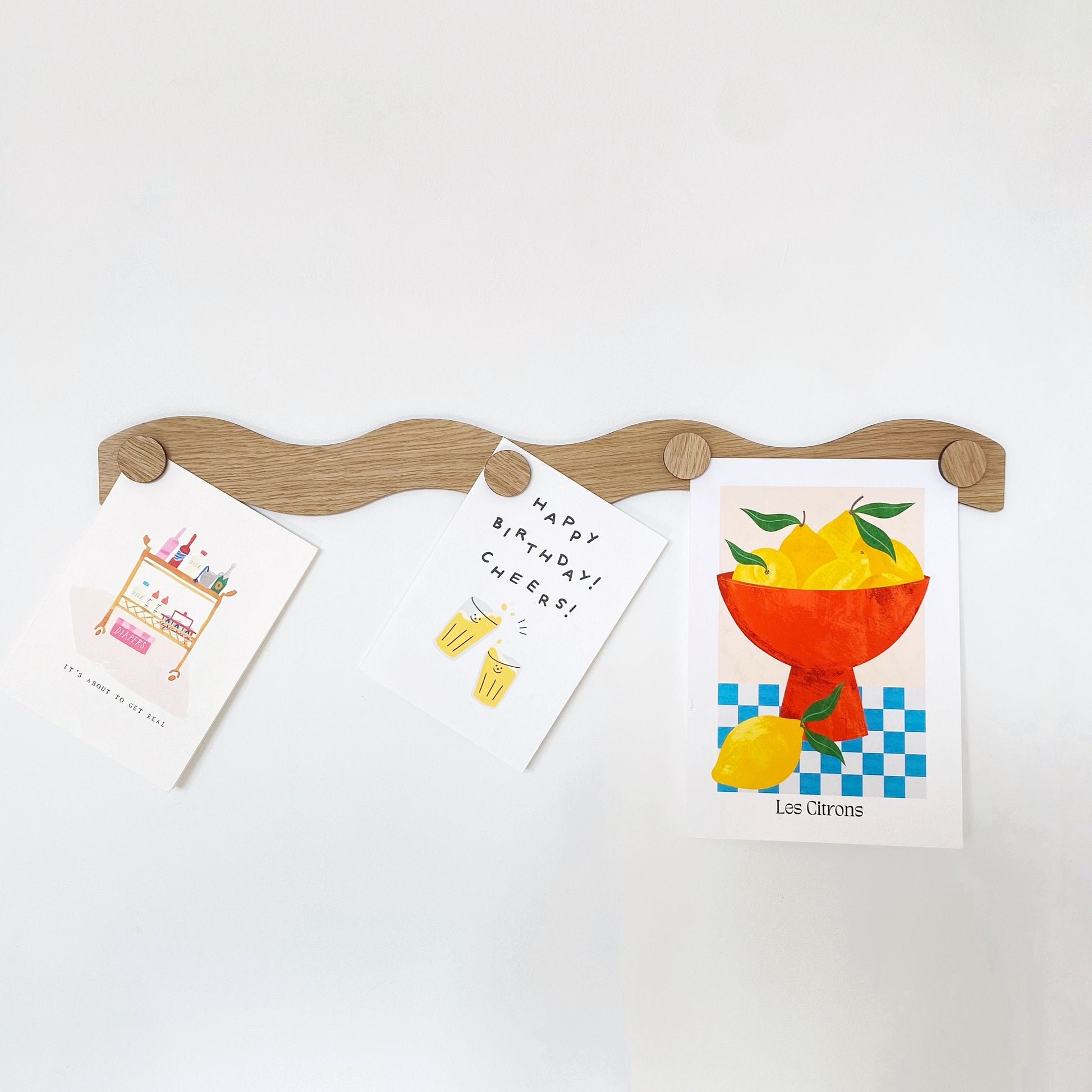 Modern wooden oak magnet display bar with a wavy design, featuring decorative magnets holding stylish cards. Perfect for organizing or displaying paper items, this unique display accessory blends function and aesthetic for home or office.