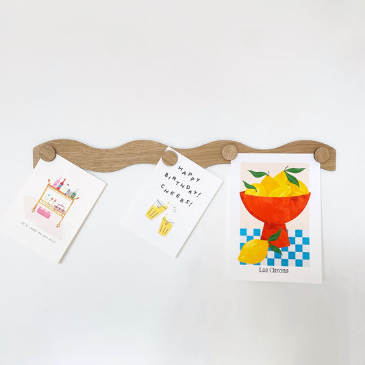 Modern wooden oak magnet display bar with a wavy design, featuring decorative magnets holding stylish cards. Perfect for organizing or displaying paper items, this unique display accessory blends function and aesthetic for home or office.