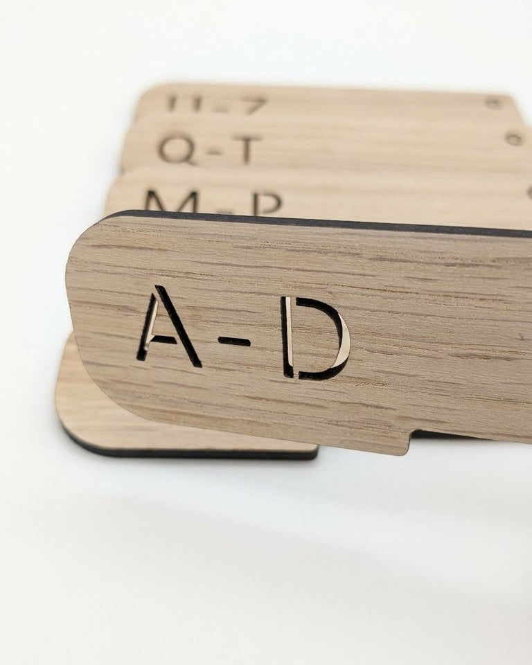 Close-up of a light natural wood desk calendar or organizer page labeled 'A-D', with additional pages stacked behind it on a white background.