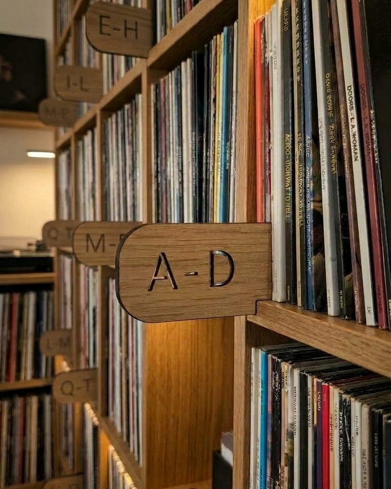 Wooden record store shelves filled with vinyl records, with a wooden sign reading A-D hanging on a shelf.