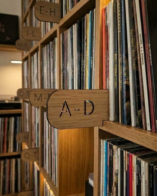 Wooden record store shelves filled with vinyl records, with a wooden sign reading A-D hanging on a shelf.